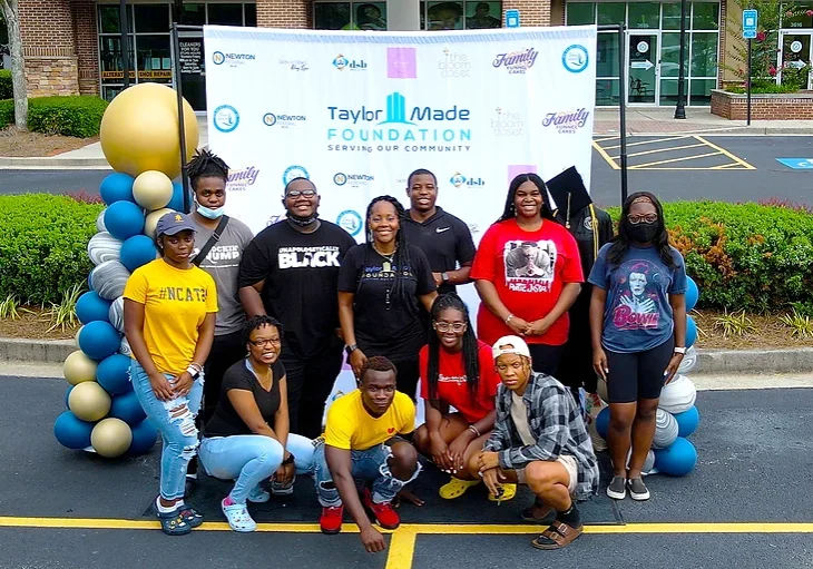 group of students standing in front of a taylor made foundation banner